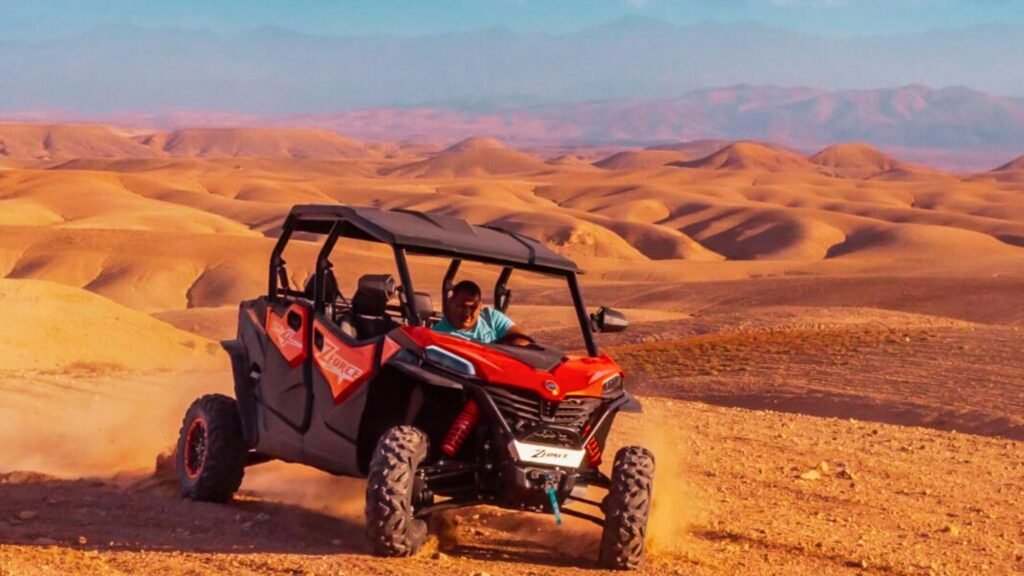 Man driving a red buggy through the rocky Agafay Desert near Marrakech with Atlas Mountains in the background