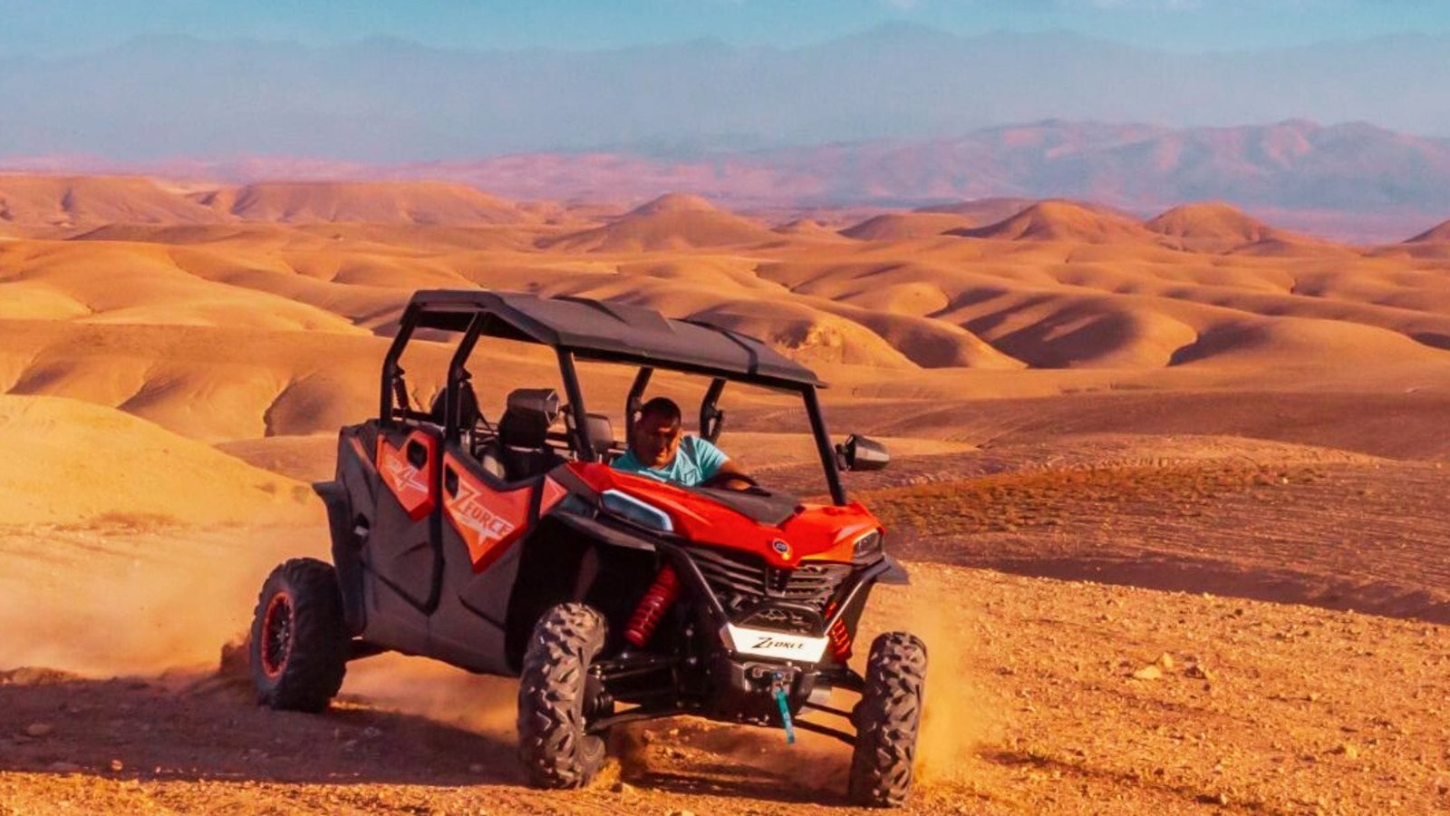 Man driving a red buggy through the rocky Agafay Desert near Marrakech with Atlas Mountains in the background