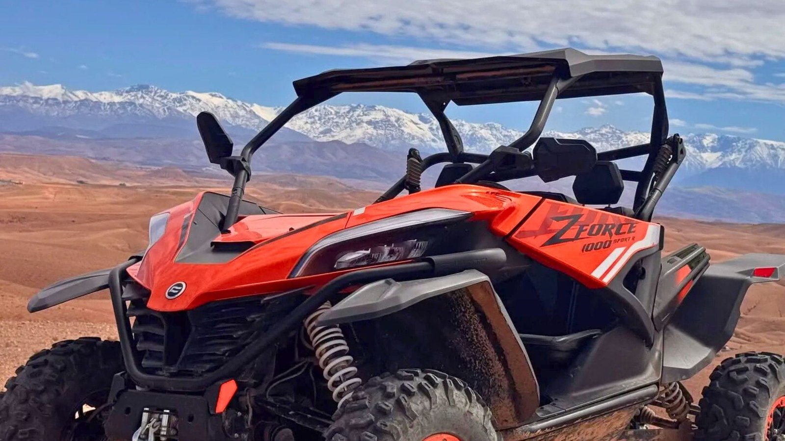 Red buggy parked on rocky desert terrain in the Agafay Desert near Marrakech with snow-capped Atlas Mountains in the background